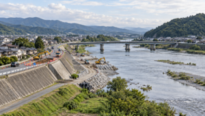道路の沈下を補修する工事現場と、橋・堤防がある日本の河川沿い