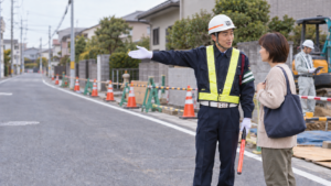 工事現場で近隣住民に迂回方向を説明する交通誘導警備員